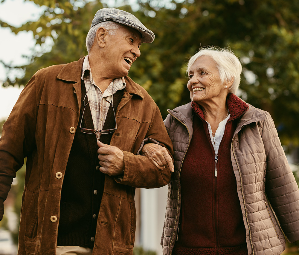 Portrait of happy retired man and woman in warm clothing walking outdoors on street. Loving senior couple enjoy a walk together on a winter day